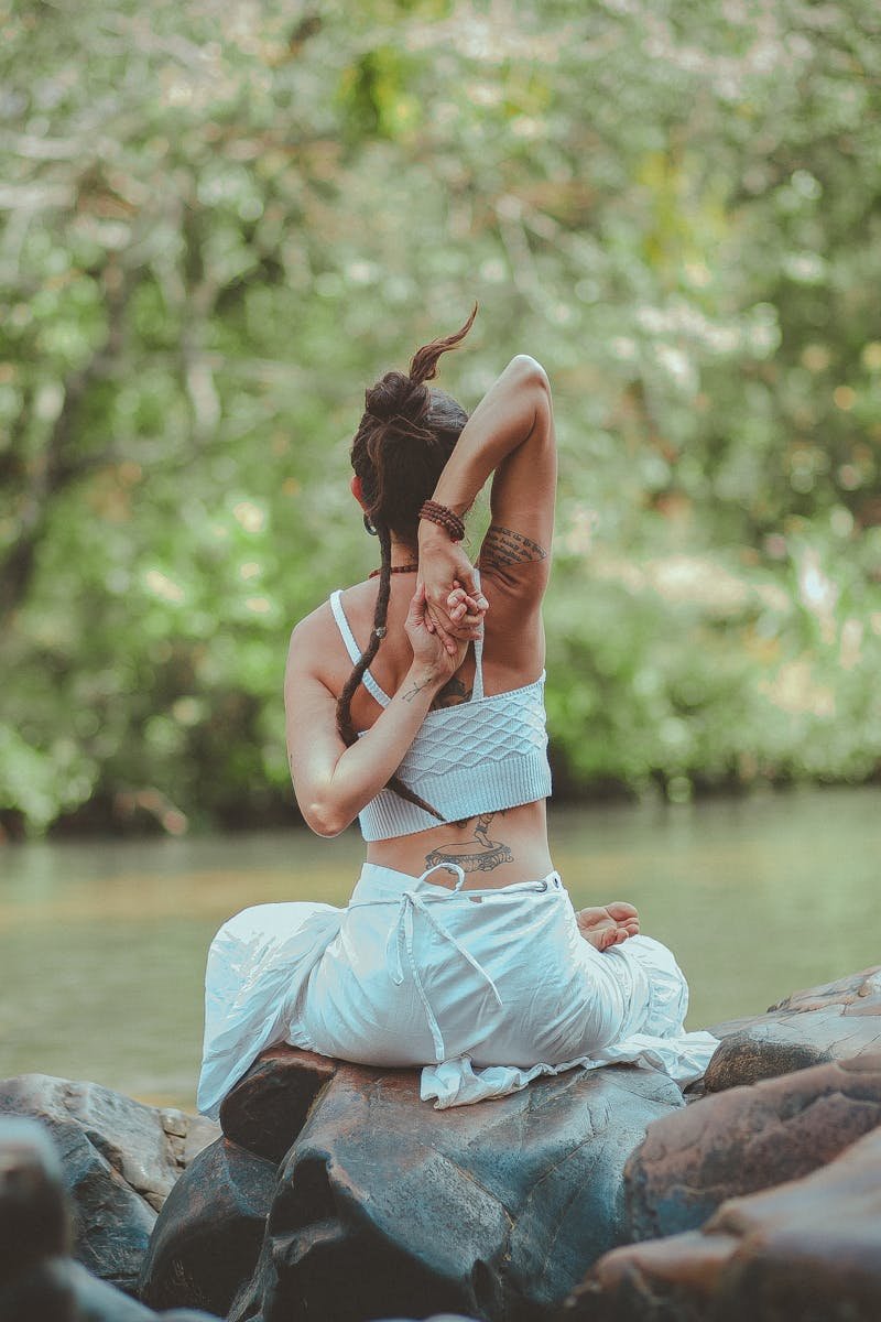 A woman in a yoga pose by a calm river, surrounded by nature, embodying peace and tranquility.